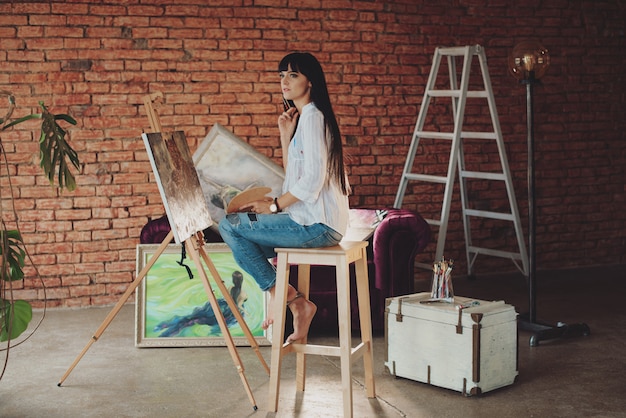 A young smiling brunette woman artist in her Studio is holding a brush.