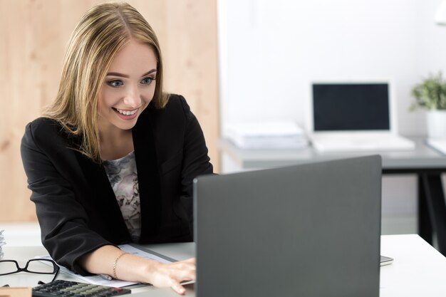 Young smiling business woman working at laptop in the office. Businesswoman chatting with someone online.