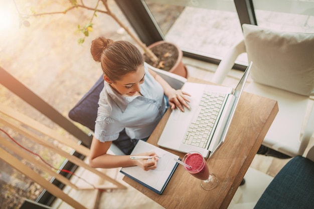 Young smiling businesswoman on a break in a cafe. She is working at laptop. Top view.