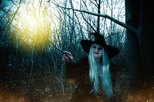 Young smiling Caucasian girl wearing a witch costume and makeup with a magic stick in the forest