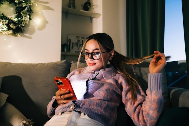 Young smiling caucasian woman using mobile phone in holidays at home on the sofa.