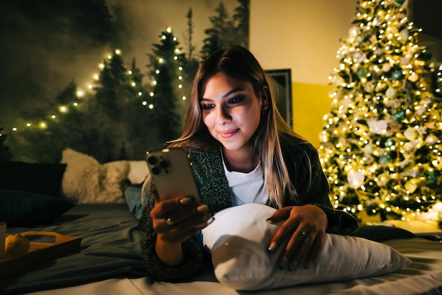 사진 휴일에 집에서 침대에서 휴대전화를 사용하여 웃고 있는 젊은 백인 여성.