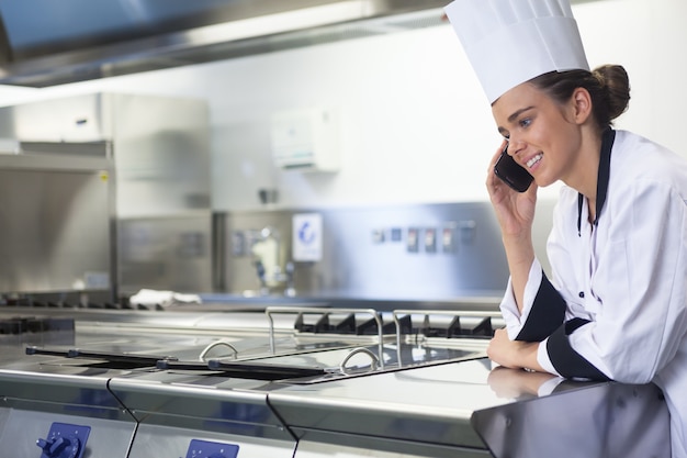 Young smiling chef standing next to work surface phoning