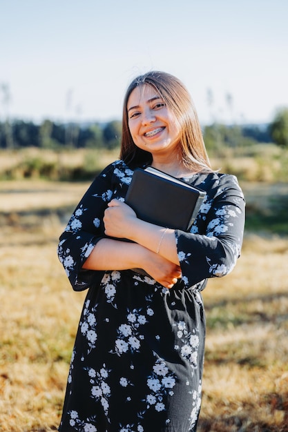 Young smiling christian girl holding a bible under her arm in the field. Sola scriptura. Copy space