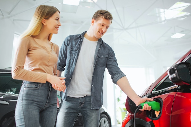Young smiling couple buying electric car in the showroom