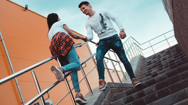 Young smiling couple in love man holding attractive woman hand, spending time together, enjoying - orange background - girl rolls on the railing