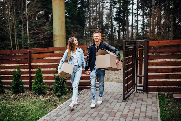 Young smiling couple with boxes on moving day. Happy homeowners or renters just moved into modern house with terrace