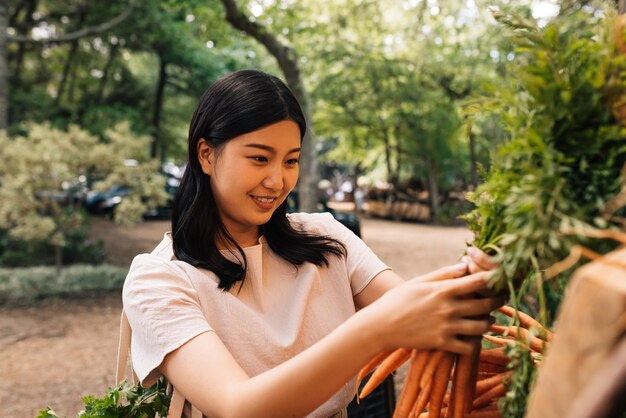 Photo young smiling customer choosing carrot on the outdoor market