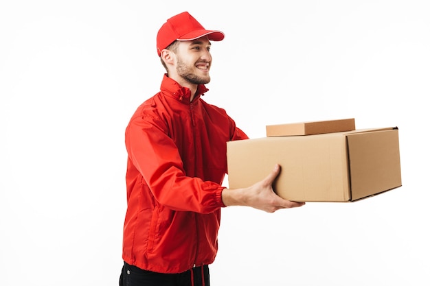 Young smiling delivery man in red cap and jacket giving boxes to customer happily