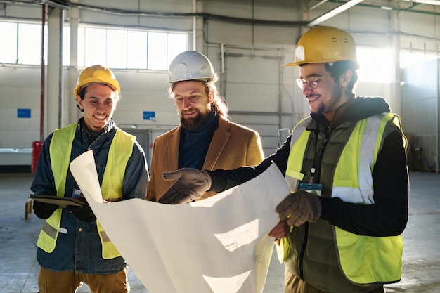 Young smiling engineer pointing at building plan in blueprint