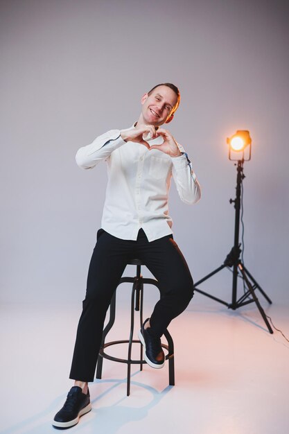 A young smiling European man in a shirt and black pants sits on a chair and smiles at the camera A stylish man in casual clothes