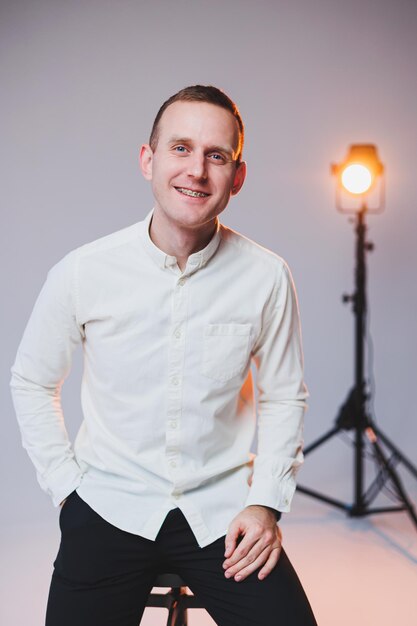 A young smiling European man in a shirt and black pants sits on a chair and smiles at the camera A stylish man in casual clothes