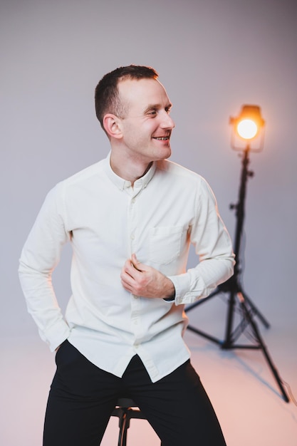 A young smiling European man in a shirt and black pants sits on a chair and smiles at the camera A stylish man in casual clothes