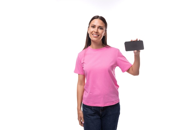 분홍색 티셔츠를 입고 검은 머리에 흉내낸 모형이 달린 스마트폰을 들고 웃고 있는 젊은 유럽 여성