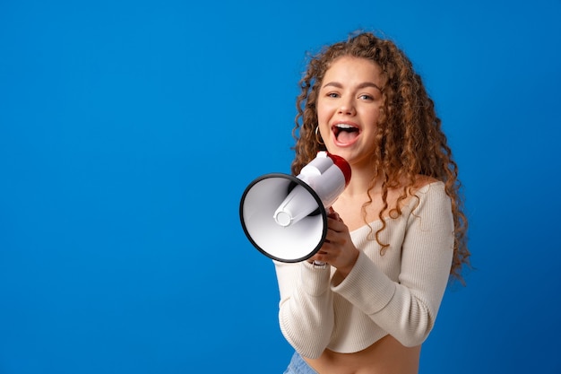 Young smiling expressive caucasian woman shout in megaphone against blue background