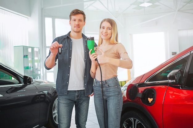 Молодая улыбающаяся семья покупает свой первый электромобиль в автосалоне