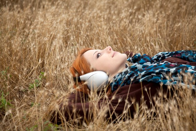 Young  smiling fashion with headphones lying at field.