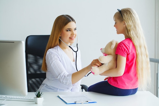 Young smiling female doctor and her little patient with teddy bear.