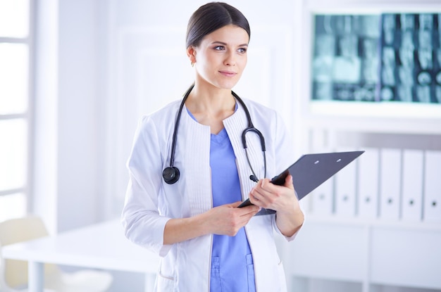 Young smiling female doctor with stethoscope holding a folder at a hospital's consulting room