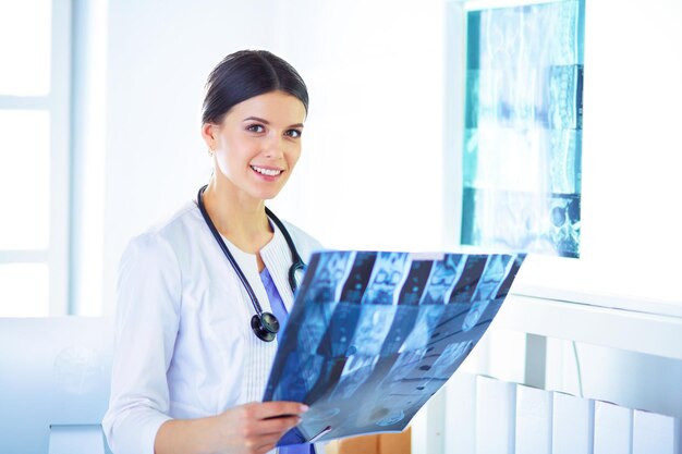 Foto giovane dottoressa sorridente con lo stetoscopio che esamina i raggi x presso l'ufficio del medico