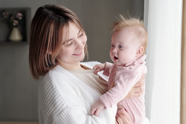 彼女の腕に愛らしい幼児を見ている若い笑顔の女性