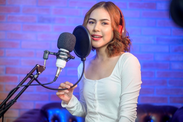 A young smiling female singer wearing headphones with a microphone while recording song