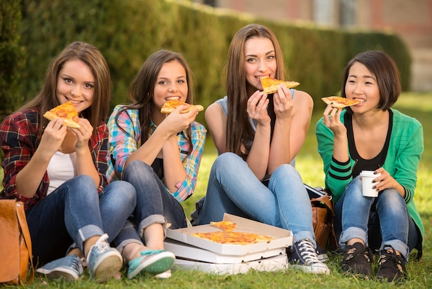 Young smiling female students are sitting on the ground.