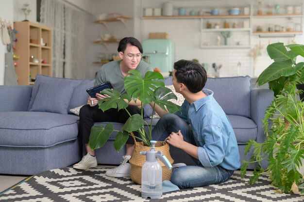 写真 自宅のリビングルームで観葉植物の世話をしている若い笑顔の同性愛者のカップル