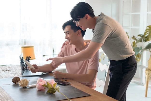 Young smiling gay couple working on new project and shooting pictures of new product by smartphone