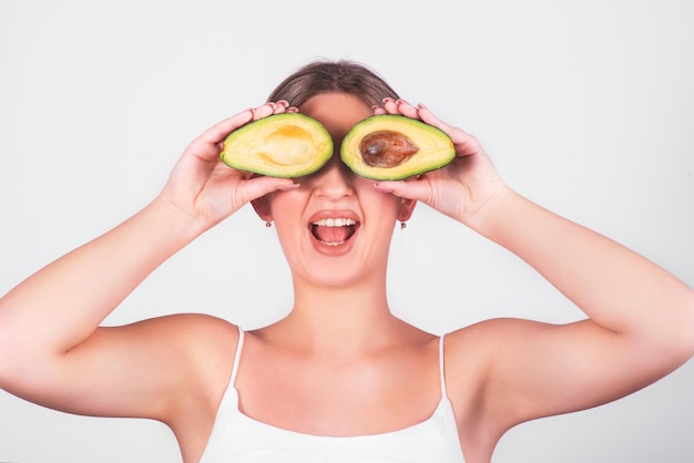 Young smiling girl of European appearance is holding avocado in front of her eye on white background