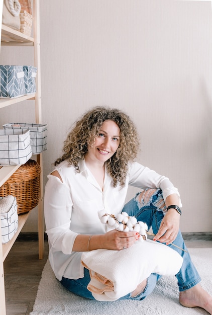 A young smiling girl in fashionable stylish spring clothes is\
sitting on the floor with a blooming sprig of cotton in her\
hands.