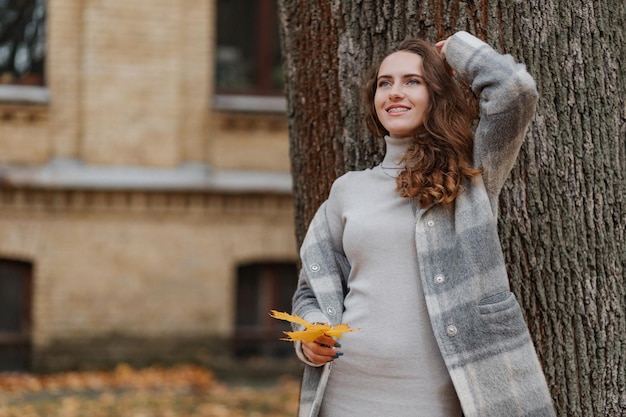 La giovane ragazza sorridente in un cappotto grigio tiene una foglia gialla nelle sue mani