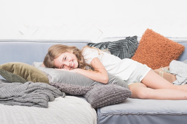 Photo young smiling girl lying on a bed with pillows holidays free time