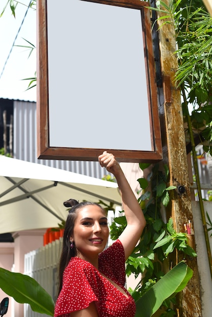 Молодая улыбающаяся девушка указывает на пустой белый знак
