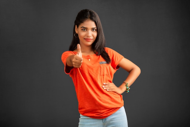 Young smiling girl showing ok sign or thumbs up on a grey background