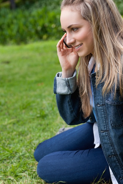 잔디에 앉아있는 동안 전화로 얘기 웃는 소녀