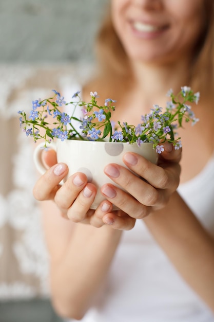 Young smiling girl in a white tank holding a dotted cup with forgetmenot Flowers in a mug