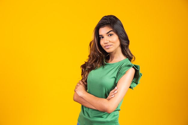 Young smiling girl with arms crossed on yellow background.