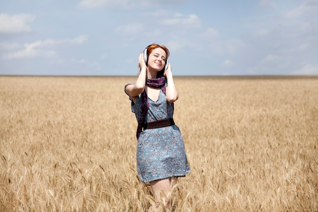 Giovane ragazza sorridente con le cuffie al campo di grano.