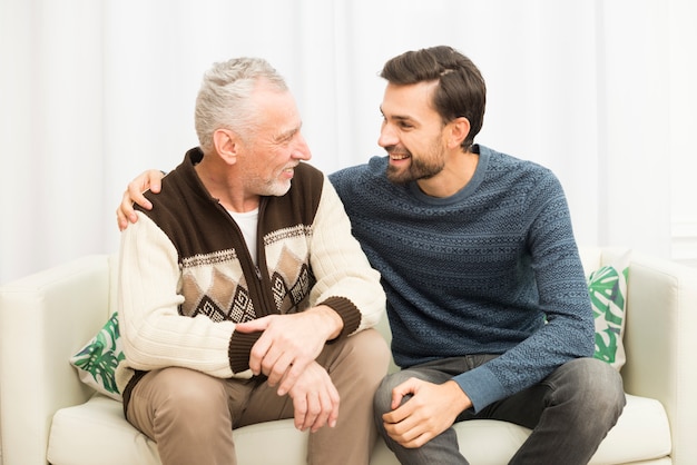 young smiling guy hugging aged man on sofa