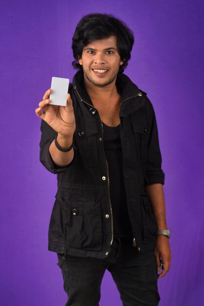 紫色の背景にクレジットカードでポーズをとって若い笑顔のハンサムな男