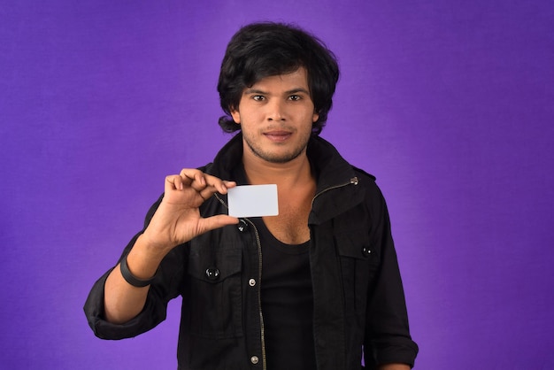 Young smiling handsome man posing with a credit card on purple background