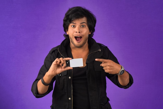 Young smiling handsome man posing with a credit card on purple background