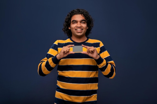 Young smiling handsome man posing with a credit or debit card on gray background