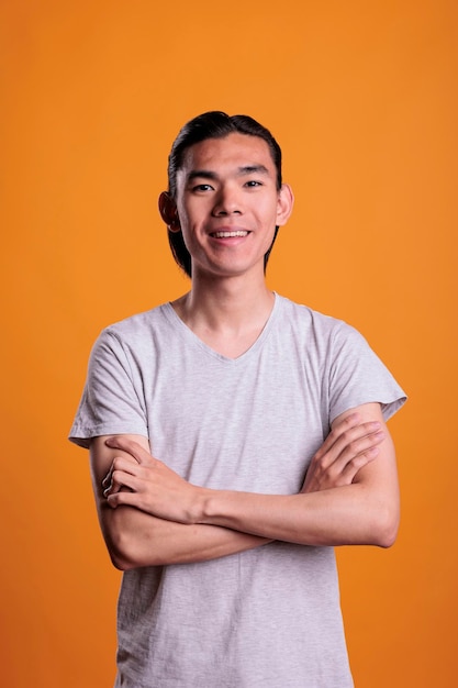 Young smiling happy asian man standing with arms crossed, looking at camera, front view. Cheerful teenager with positive facial expression portrait, attractive person medium shot