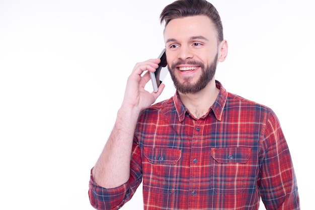 Young smiling happy cheerful bearded man in plaid shirt talks on mobile or cell phone conducting pleasant conversation with friend