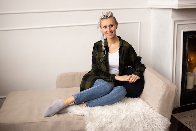 Young smiling hipster woman with dreadlocks at home on sofa