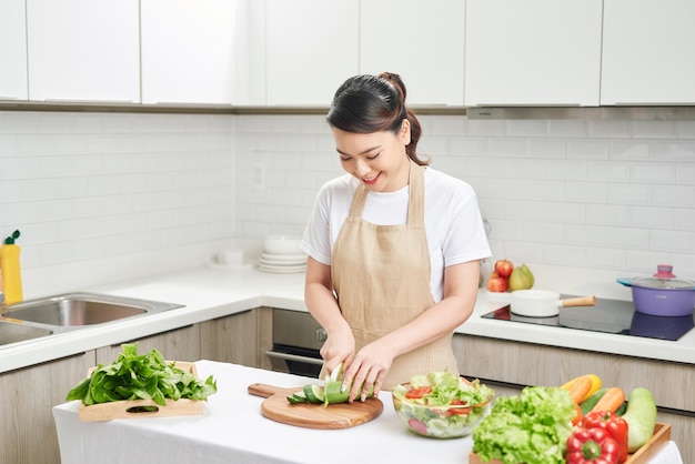 明るいモダンなキッチンで野菜と健康的な食事を準備する若い笑顔の主婦