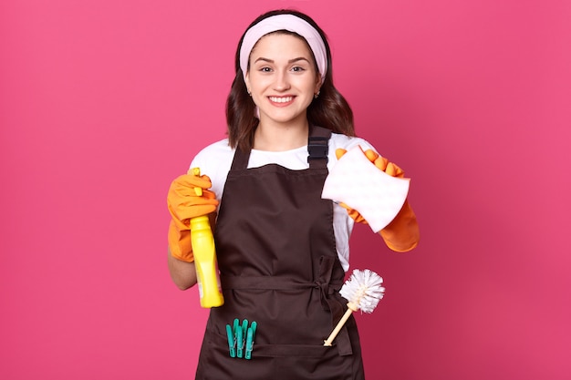 Young smiling housewife wearing hair band, brown apron and white casual t-shirt