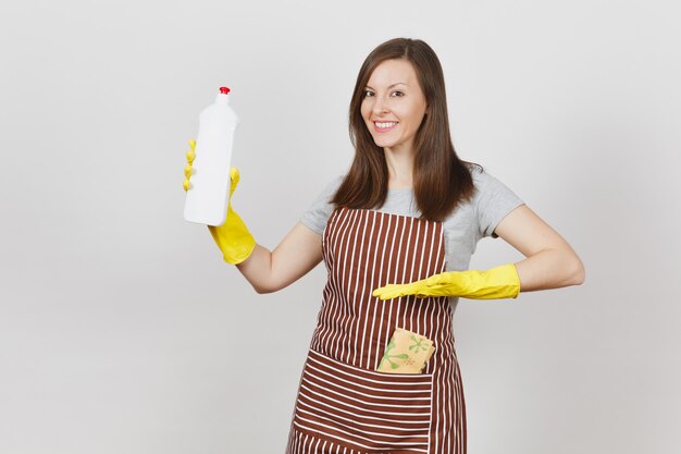 Young smiling housewife in yellow gloves, striped apron cleaning rag in pocket isolated on white background. Woman holding and pointing hand on bottle with cleaner liquid. Copy space for advertisement